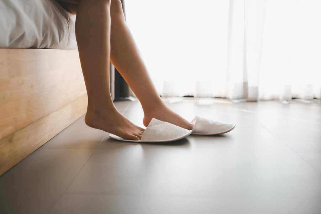 A person sitting on the edge of a bed, putting on slippers.