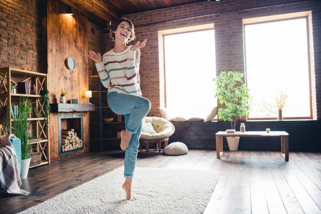 A happy person dancing on a rug in the middle of a modern, exposed-brick living room.